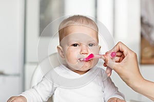 Feeding of cute baby with a spoon in the kitchen