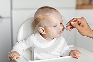 Feeding of cute baby with a spoon in the kitchen