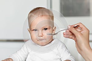 Feeding of cute baby with a spoon in the kitchen