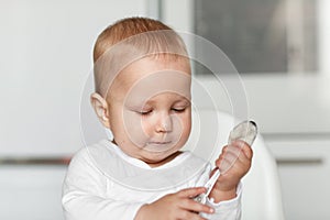 Feeding of cute baby with a spoon in the kitchen