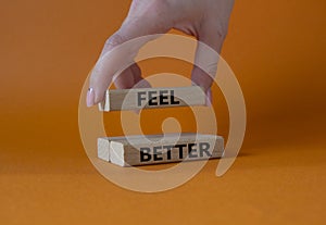 Feel better symbol. Wooden blocks with words Feel better. Businessman hand. Beautiful orange background. Business and Feel better