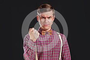 Feeling so angry! Angry young man in vintage shirt and bow tie with hairstyle looking at camera and making a face and show a fist