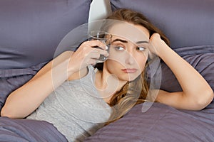 Feeling bad from a hangover in the morning : young woman hold glass of water and lying in bed bedroom