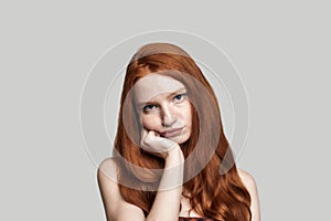 Feeling boring. Portrait of frustrated girl with red hair making sad face while standing against grey background