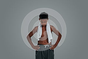 Feeling exausted after workout. Half teenage african boy with towel on shoulders keeping head down while standing photo