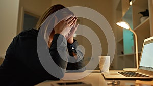 Feeling exhausted. Tired young woman looking at laptop screen, sitting at her working place in the evening at home