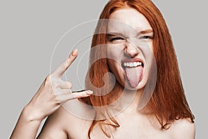 Feeling free. Close up portrait of young and cute teenage girl with long red hair showing hand sign and sticking out