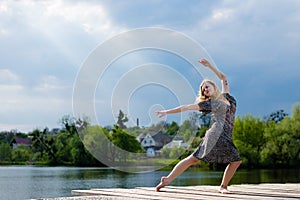 Feeling free: portrait of young beautiful blond lady dancing girl with falling sun lighting rays from blue sky at water lake