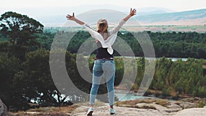 Feeling of freedom and happiness, a sweet and slender young woman standing on a cliff, and raising her arms upwards