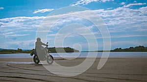 The feeling of freedom and Moto aesthetics. Motorcyclist riding on his bike on sandy beach.