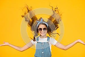 Feeling good fabulous hair. Adorable girl with curly hair waving on yellow background. Little hair model with fashion