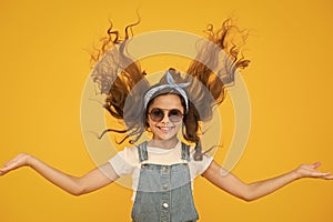 Feeling good fabulous hair. Adorable girl with curly hair waving on yellow background. Little hair model with fashion