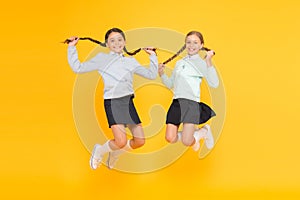 Feeling good fabulous hair. Cute small children with plaited hair jumping on yellow background. Happy little girls