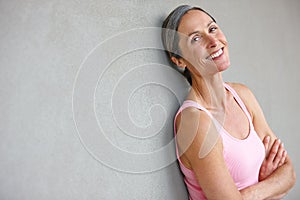 Feeling great. Portrait of an attractive mature woman in gymwear leaning against a gray wall.