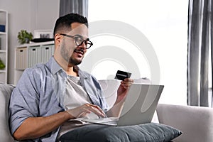 Feeling happy and confident. Young Asian man using laptop computer holding credit card for online shopping and payment at home