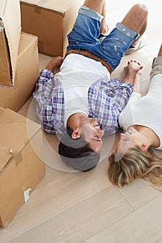 Feeling at home. A happy young couple looking at each other lovingly while lying on the floor in their new home.