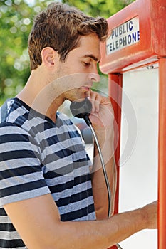 Feeling home sick - Travel. Profile of a handsome young man using a public telephone.