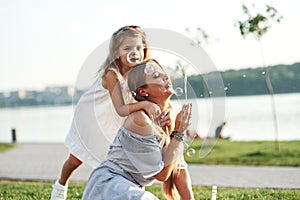 Feeling peaceful. Photo of young mother and her daughter having good time on the green grass with lake at background