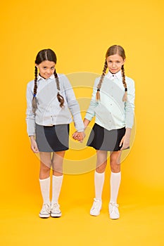 Feeling shy. Cute children holding hands on yellow background. Little children wearing school uniform. School children