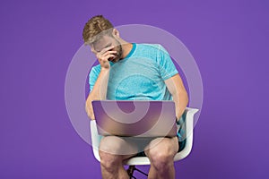 Feeling sick and tired. Frustrated young man covering face with hands while sitting with laptop. Man surfing internet on