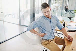 Feeling the strain of a long day at his desk. Cropped shot of a young businessman experiencing back pain while working