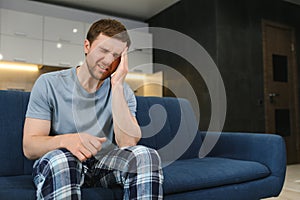 Feeling stressed. Frustrated handsome young man touching his head and keeping eyes closed while sitting on the couch at