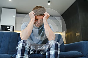 Feeling stressed. Frustrated handsome young man touching his head and keeping eyes closed while sitting on the couch at