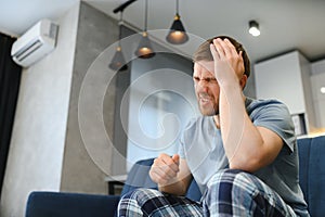 Feeling stressed. Frustrated handsome young man touching his head and keeping eyes closed while sitting on the couch at