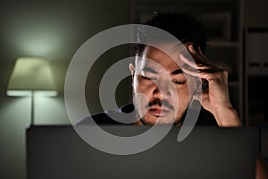 Feeling stressful and depressed. Asian man feeling looking unhappy, stressed and tired while using computer working late at night