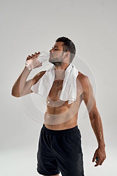 Feeling thirsty after workout. Vertical shot of young handsome muscular man with towel on his shoulders drinking water