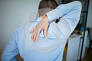 Feeling tired. Back view of frustrated young man looking exhausted and massaging his neck while sitting at workplace