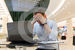 Feeling tired. Frustrated young man covering his face with hands while working on laptop