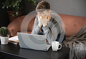 Feeling tired.Frustrated young  man student looking exhausted and covering his face with hands while sitting at laptop