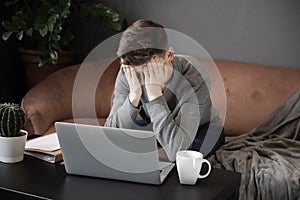 Feeling tired.Frustrated young  man student looking exhausted and covering his face with hands while sitting at laptop