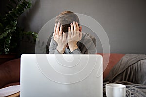Feeling tired.Frustrated young  man student looking exhausted and covering his face with hands while sitting at laptop