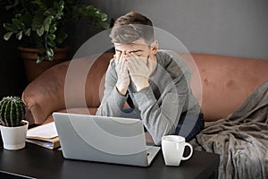 Feeling tired.Frustrated young  man student looking exhausted and covering his face with hands while sitting at laptop