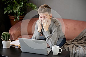 Feeling tired.Frustrated young  man student looking exhausted and covering his face with hands while sitting at laptop