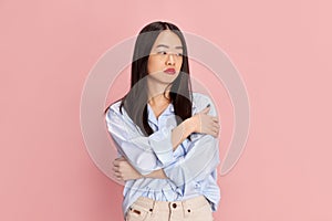 Feeling tired. Portrait of young beautiful girl in casual clothes posing with emotionless face against pink studio