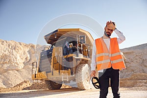 Feeling tired. Standing against haul truck. Man in uniform is working in the quarry at daytime