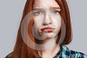 Feeling upset. Close up of offended girl with red hair making sad face while standing against grey background