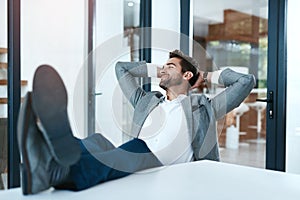 That feeling after youve slayed all day. a handsome young businessman relaxing with his feet up on a desk in a modern