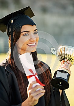 Feels great to be recognized as a top achiever. Portrait of a student holding her diploma and trophy on graduation day.