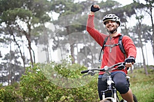 This feels great. A young male athlete pumping his fist in the air after conquering a mountain biking trail.