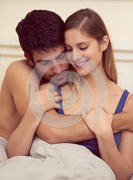 It feels so right when you hold me tight. Shot of a loving young couple sharing an intimate embrace while sitting in bed