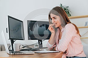 Feels worried. Female stock broker in casual clothes is working in the office by pc