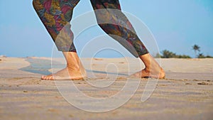 Feet of active senior woman practicing tai chi gymnastic on sandy beach.