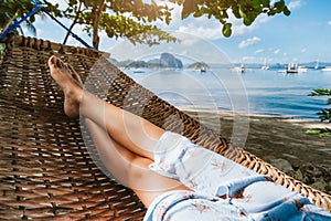 Feet of adult woman relaxing in a hammock on the beach during summer holiday