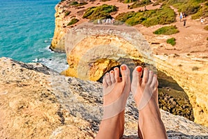 feet against a cliff on the famous Benagil beach in Portugal, waves crashing on the rocks, the raging ocean