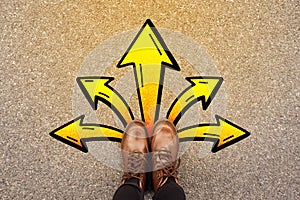 Feet and arrows on road background. Top view. Selfie woman in leather ankle boots on pathway with yellow graffiti arrow sign photo