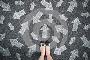 Feet and arrows on road background. Woman standing with many direction sign arrow choices in different ways, left and forward.